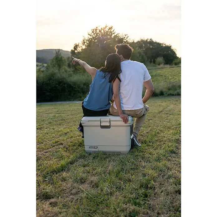 Coleman Kühlbox Pro 55QT - L x B x H: 65 x 37 x 48 cm, Schwarz, 52 l - Ein Paar sitzt auf einer Coleman 100 PRO Kühlbox im Freien, genießt die Aussicht und die Natur. Die Kühlbox bietet Komfort und Funktionalität.