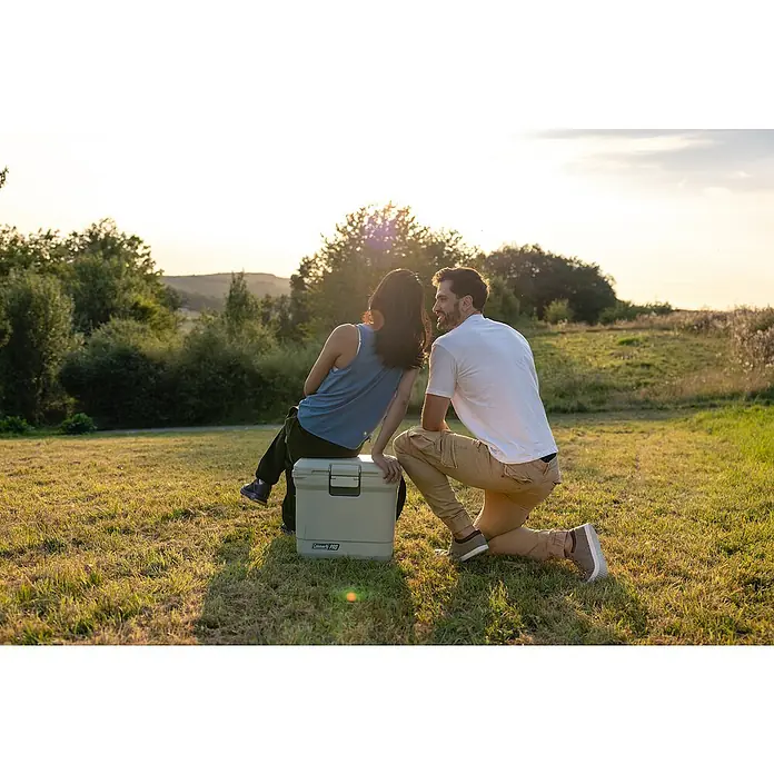 Coleman Kühlbox Pro 25QT - L x B x H: 35 x 45 x 45 cm, Weiß, 24 l - Ein Paar entspannt auf einer Wiese mit einer Coleman Kühlbox. Die Kühlbox ist ideal für Outdoor-Abenteuer und hält Getränke kühl.