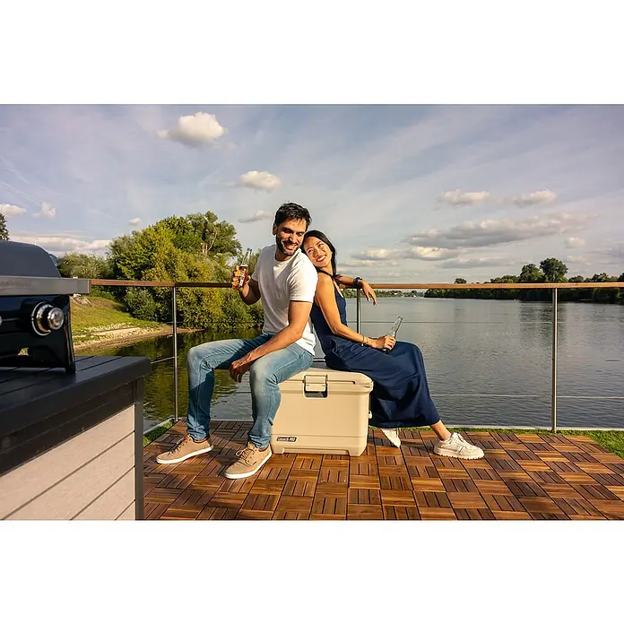 Coleman Kühlbox Pro 55QT - L x B x H: 65 x 37 x 48 cm, Schwarz, 52 l - Ein Paar entspannt auf einem Coleman Kühlbox am Fluss, mit Getränken in der Hand. Die Kühlbox hält Speisen und Getränke kühl.