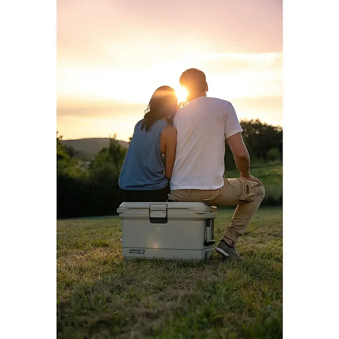 Coleman Kühlbox Pro 45QT - L x B x H: 26 x 47 x 43 cm, Schwarz, 42,5 l - Ein Paar sitzt auf einer Coleman PRO Kühlbox im Freien bei Sonnenuntergang und genießt die Aussicht. Die hochwertige Kühlbox hält Getränke und Speisen kühl.