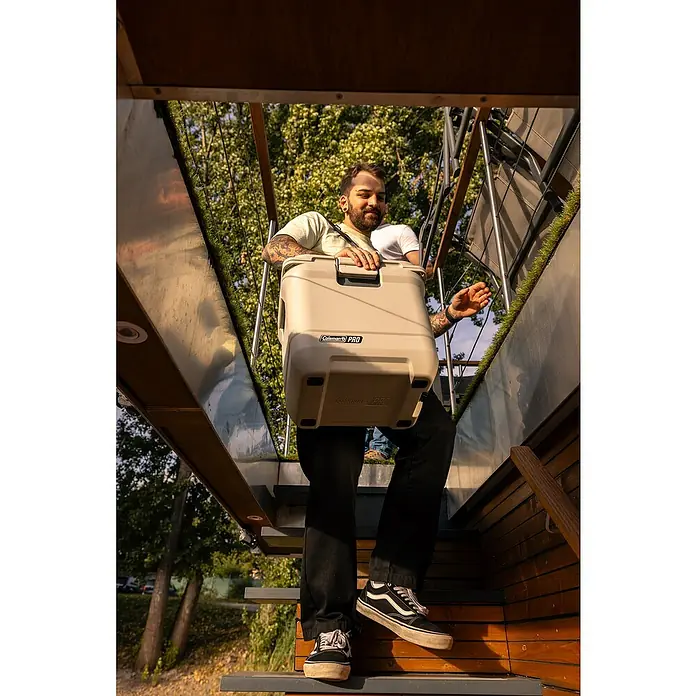 Coleman Kühlbox Pro 25QT - L x B x H: 35 x 45 x 45 cm, Weiß, 24 l - Mann trägt eine Coleman Pro Kühlbox auf einer Treppe. Die robuste Kühlbox ist ideal für Outdoor-Abenteuer und hält Speisen und Getränke kühl.