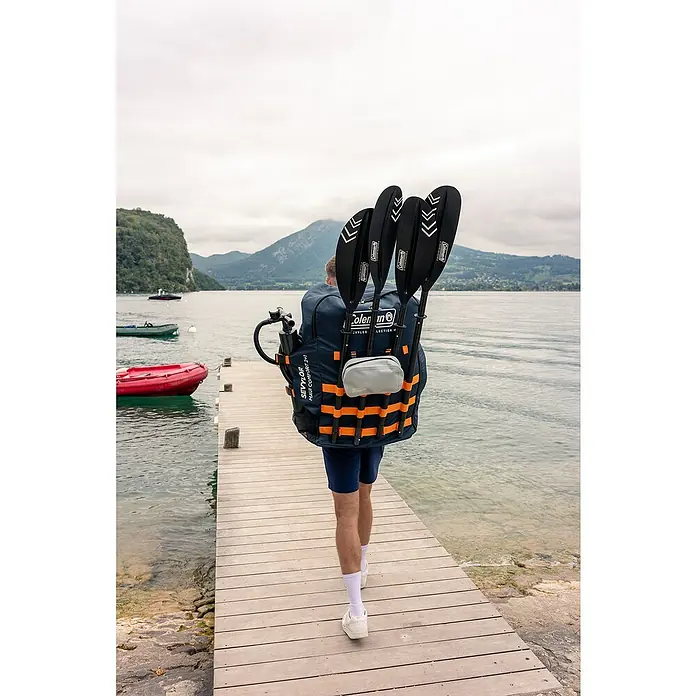Sevylor Kajak Maui 2 + 1 - L x B: 380 x 98 cm, Nutzlast: 250 kg, Geeignet für: 2+1 Personen - Person mit Coleman Kajak-Paddeln auf dem Rücken, die auf einem Holzsteg am See entlanggeht. Perfekt für Outdoor-Abenteuer und Wassersport.