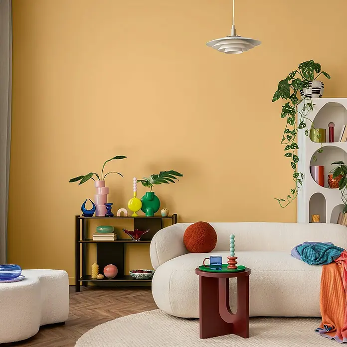 swingcolor Wandfarbe SIMPLY - Nr. 25, 1 l - Wohnzimmer mit einem weißen Sofa, einem Beistelltisch und bunten Dekorationsgegenständen vor einer gelben Wand.