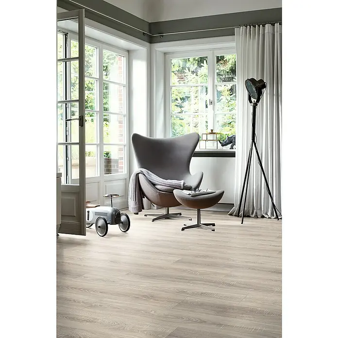 Egger Laminat NatureSense Aqua - Toscolano Eiche hell, Landhausdiele, 1.292 x 193 x 8 mm - Zimmer mit einem grauen Sessel und einem grauen Spielzeugauto auf einem Holzboden. Die Fenster sind hell und lichtdurchflutet.
