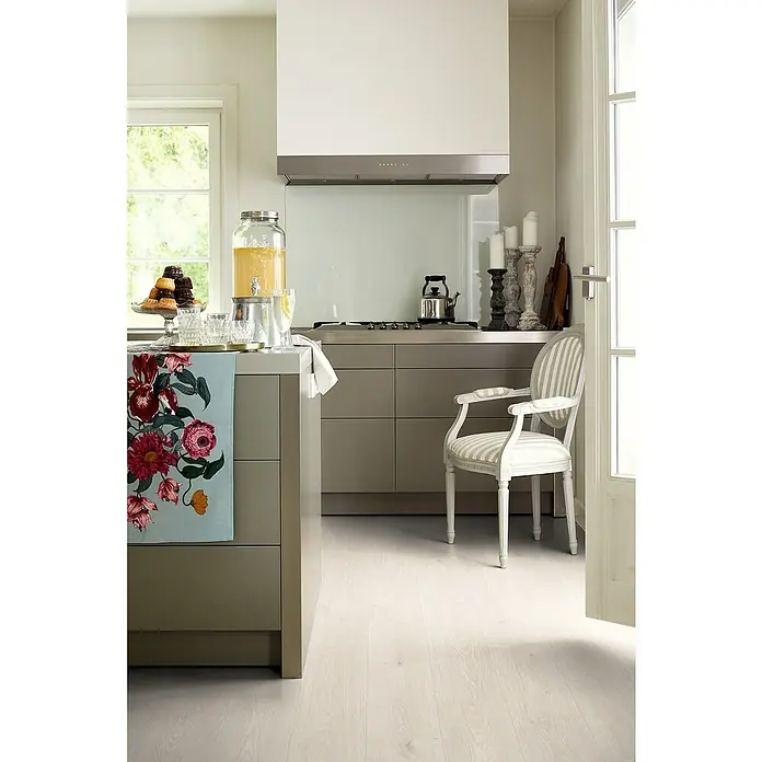 Egger Laminat Aquadura+ - Camden Eiche weiss, Landhausdiele, 1.292 x 193 x 7,5 mm - Helle Küche mit Kücheninsel, Getränkespender und einem eleganten Stuhl mit Streifenmuster.