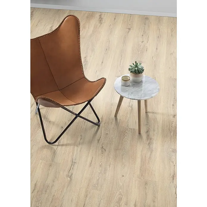 Egger Laminat Aquadura+ - Panora Eiche beige, Landhausdiele, 1.292 x 193 x 7,5 mm - Einrichtungsszene mit einem braunen Ledersessel und einem kleinen Marmortisch mit einer Sukkulente auf einem hellen Holzboden.