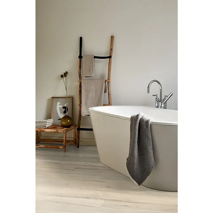 Egger Laminat Aquadura+ - Halifax Eiche weiss, Landhausdiele, 1.292 x 193 x 7,5 mm - Modernes Badezimmer mit freistehender Badewanne, Handtuchleiter und stilvollen Textilien in neutralen Farbtönen für eine entspannende Atmosphäre.