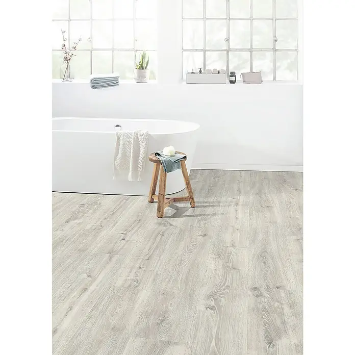 Egger Laminat Aquadura+ - Waltham Eiche weiss, Landhausdiele, 1.292 x 246 x 7,5 mm - Badezimmer mit einem freistehenden, weißen Bad, einem Holzhocker mit Handtuch und einem hellen Holzboden für eine entspannende Atmosphäre.