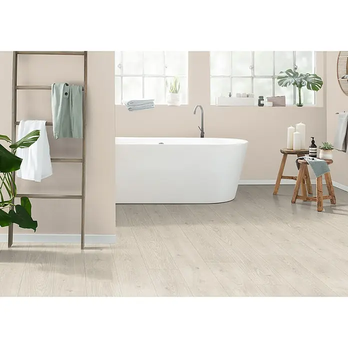 Egger Laminat Aquadura+ - Berdal Eiche weiss, Landhausdiele, 1.292 x 193 x 7,5 mm - Ein Badezimmer mit einer freistehenden Badewanne, einem Holzboden und einem Handtuchhalter. Die sanften Farben schaffen eine entspannende Atmosphäre.