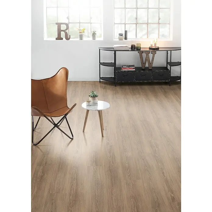 Egger Laminat Aquadura+ - Capri Eiche braun, Landhausdiele, 1.292 x 193 x 7,5 mm - Eine Inneneinrichtung mit einem braunen Ledersessel, einem kleinen Tisch mit Marmorplatte und einer schwarzen Kommode.