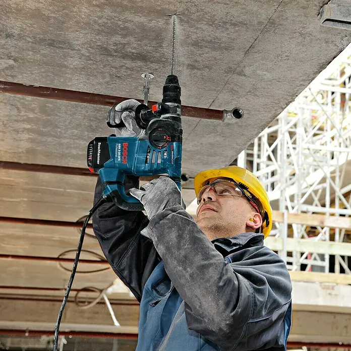 Bosch Professional Bohrhammer GBH 3-28 DFR - 800 W, 3,1 J, SDS-Plus-Aufnahme - Ein Bauarbeiter bohrt mit einem Bosch Bohrhammer Löcher in eine Betondecke, wobei er Schutzkleidung trägt.