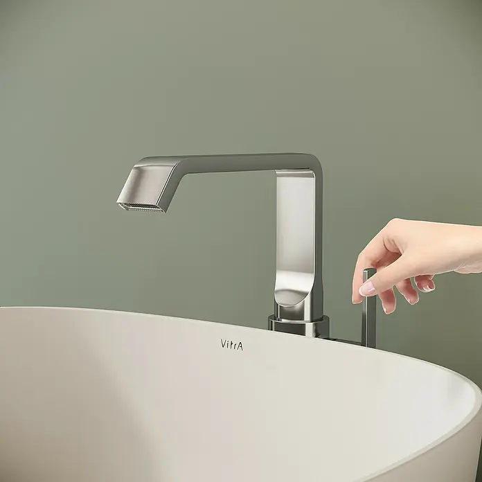 VitrA Suit Waschtischarmatur - Chrom, Glänzend, Ohne Zugstange, Höhe: 25,7 cm - Eine Hand bedient einen modernen Chrom-Wasserhahn auf einem weißen Waschbecken.