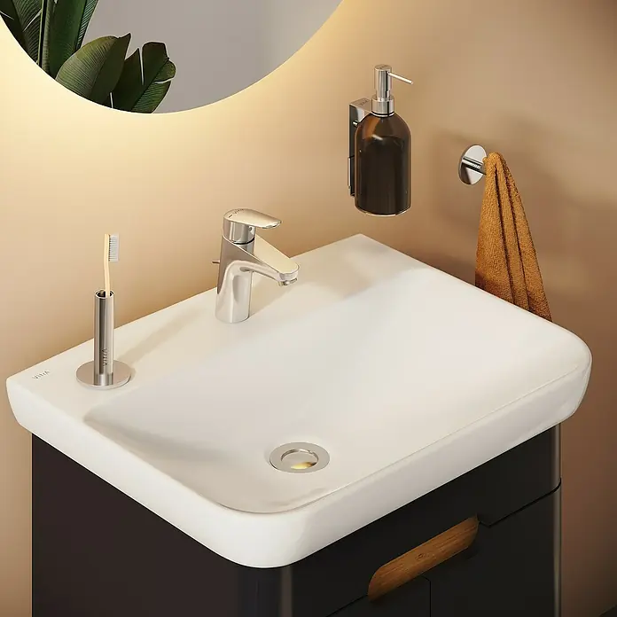 VitrA Flow Round Waschtischarmatur - Höhe: 15 cm, Ausladung Armatur: 114 mm, Chrom, Mit Zugstange - Moderner Badezimmerwaschtisch mit weißem Rechteckwaschbecken, Chromarmatur, Wandseifenspender und Zahnbürstenhalter, auf dunklem Schrank.