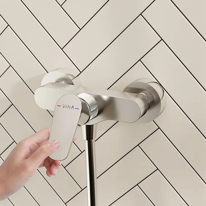 VitrA Flow Soft Brausearmatur - Ausladung: 12,7 cm, Chom, Glänzend - Eine Hand bedient einen VitrA Duschmischer aus gebürstetem Metall mit roten und blauen Anzeigen.