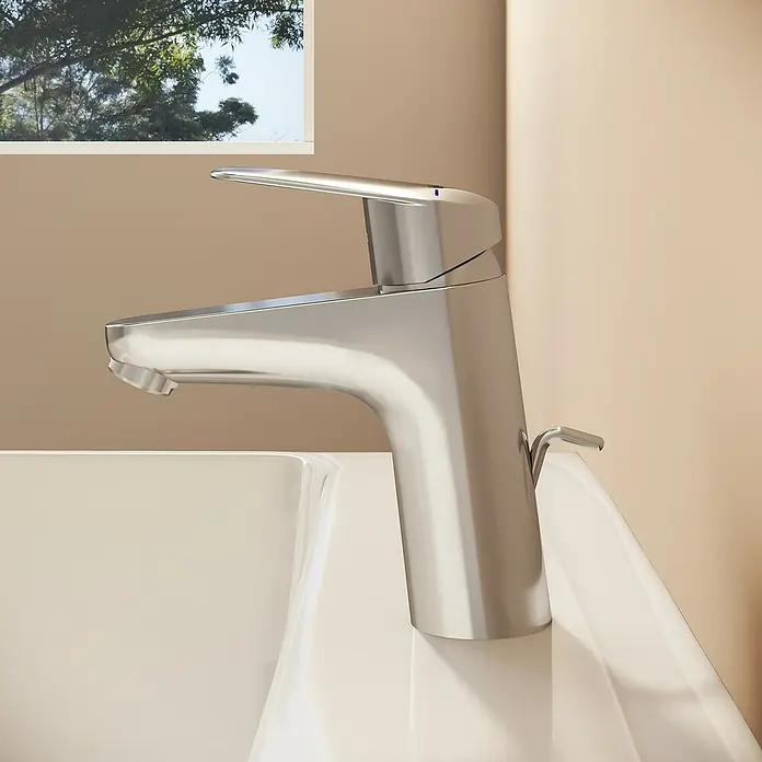 VitrA Flow Round Waschtischarmatur - Höhe: 15 cm, Ausladung Armatur: 114 mm, Chrom, Mit Zugstange - Glänzende Chromarmatur auf einem weißen Waschbecken in einem Badezimmer mit Fensterblick.