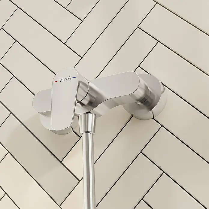 VitrA Flow Soft Brausearmatur - Ausladung: 12,7 cm, Chom, Glänzend - Verchromte Vitra Duscharmatur an einer hellen Wand mit Fischgrätmuster-Fliesen.