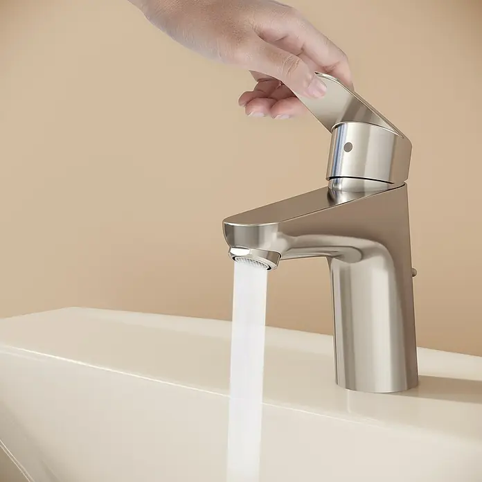 VitrA Flow Round Waschtischarmatur - Höhe: 15 cm, Ausladung Armatur: 114 mm, Chrom, Mit Zugstange - Hand dreht gebürsteten Chromhahn auf, Wasser fließt in helles Waschbecken.