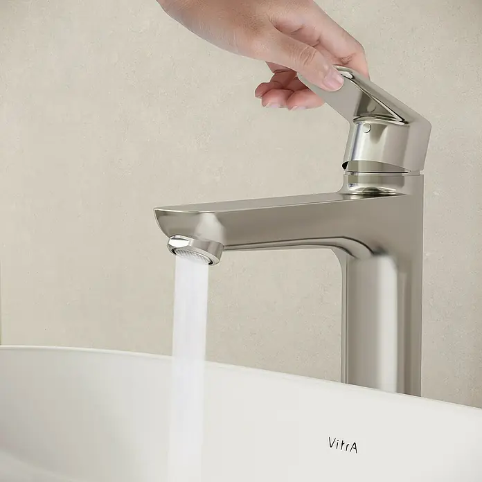VitrA Flow Soft Waschtischarmatur - Höhe: 29,3 cm, Mit Zugstange, Chrom - Verchromter Wasserhahn, dessen Griff von einer Hand betätigt wird, während Wasser in ein weißes Waschbecken läuft.