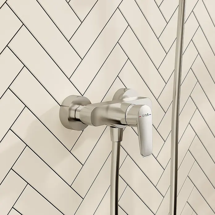 VitrA Flow Soft Brausearmatur - Ausladung: 12,7 cm, Chom, Glänzend - Ein verchromter Duschmischer mit „VitrA“-Logo am Griff, montiert an einer weiß-Fischgrät-gefliesten Wand. Ein Metall-Duschschlauch erstreckt sich nach unten.