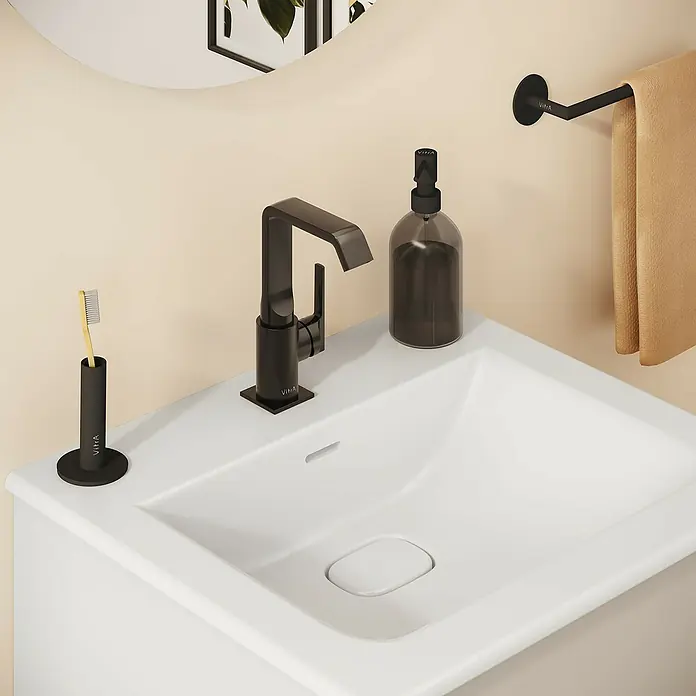 VitrA Suit Waschtischarmatur - Schwarz, Glänzend, Mit Zugstange, Höhe: 20,6 cm - Modernes Badezimmer mit weißem Waschbecken, mattschwarzem VitrA Wasserhahn, Seifenspender und Zahnbürstenhalter, sowie beigem Handtuch.