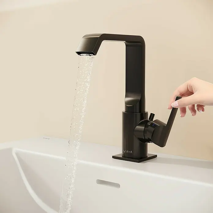 VitrA Suit Waschtischarmatur - Schwarz, Glänzend, Mit Zugstange, Höhe: 20,6 cm - Schwarze VitrA Armatur mit Wasserfluss in weißem Waschbecken, eine Hand verstellt den Griff.