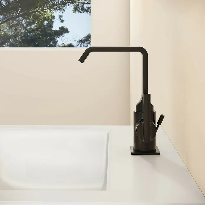 VitrA Suit Waschtischarmatur - Schwarz, Glänzend, Mit Zugstange, Höhe: 20,6 cm - Mattschwarze Küchenarmatur auf weißer Arbeitsplatte neben Spüle, mit beiger Wand und Fenster mit Bäumen im Hintergrund.