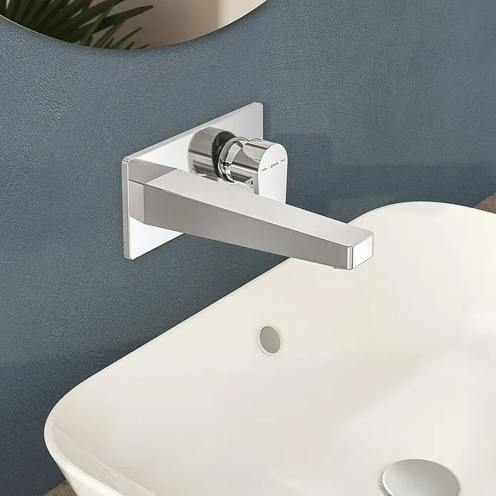 VitrA Flow Square Waschtischarmatur - Chrom, Glänzend, Ausladung Armatur: 212 mm - Verchromter Wandarmatur über einem weißen Waschbecken, vor einer strukturierten blauen Wand.