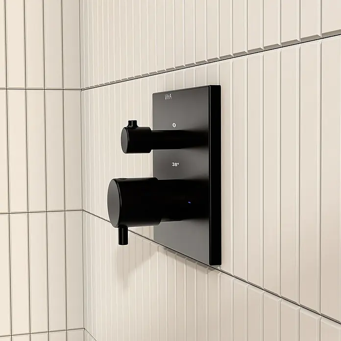 VitrA Flow Square UP-Badewannenarmatur - Ausladung Armatur: 89 mm, Schwarz, Matt - Schwarzer digitaler Duschthermostat von VitrA mit zwei zylindrischen Bedienelementen und 38°C Anzeige, montiert an einer cremefarbenen Fliesenwand.