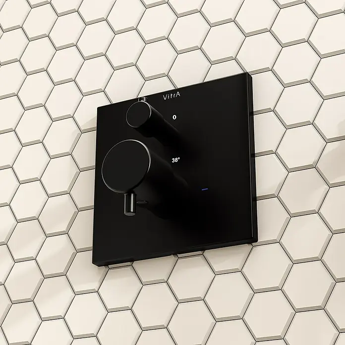 VitrA Flow Square UP-Badewannenarmatur - Ausladung Armatur: 91 mm, Schwarz, Matt - Schwarzes VitrA Duschthermostat mit zwei runden Knöpfen, Anzeige '0' und '38°', an weißer Sechseckfliesenwand.
