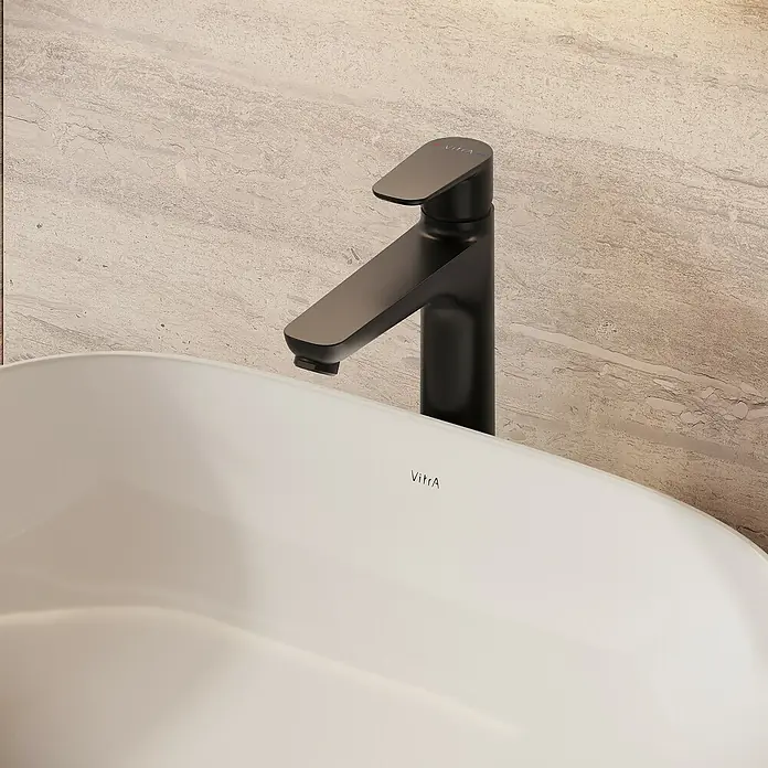 VitrA Flow Soft Waschtischarmatur - Höhe: 29,3 cm, Mit Zugstange, Schwarz - Nahaufnahme einer eleganten schwarzen Armatur über einem weißen VitrA Waschbecken vor heller Marmorwand.