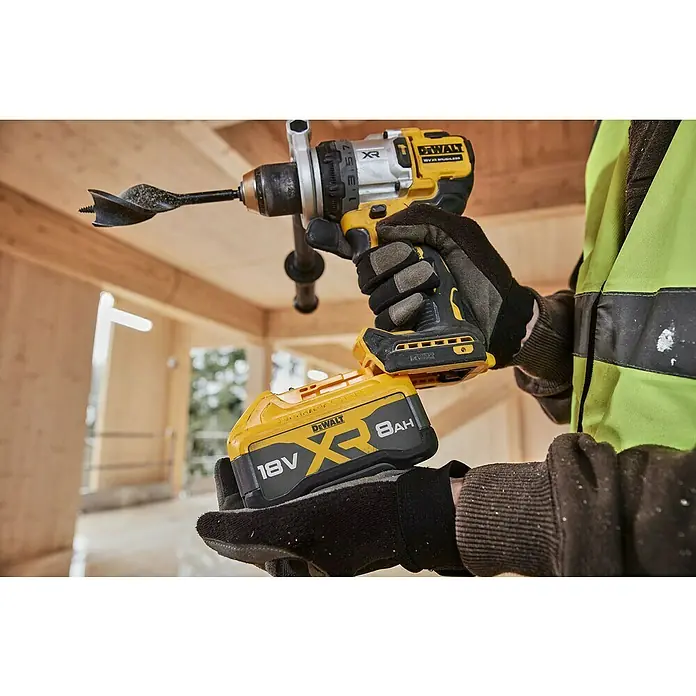 DeWalt XR 18V Taladro atornillador percutor de batería DCD1007W -  - Primer plano de un taladro inalámbrico DeWalt XR con una batería grande de 8Ah y una broca para madera, sostenido por una persona en ropa de trabajo.