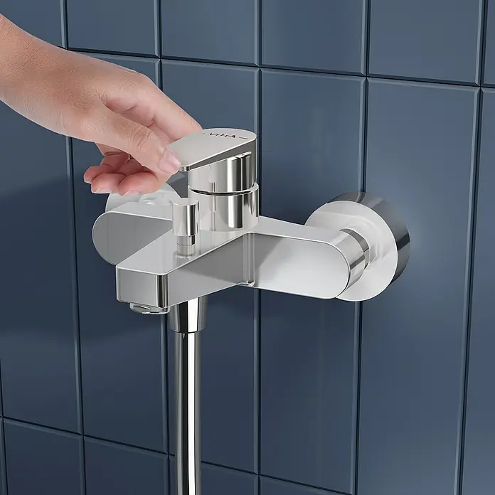 VitrA Flow Square Badewannenarmatur - Chrom, Glänzend - Eine Hand verstellt einen verchromten Duschmischerhahn an einer blau gefliesten Wand.