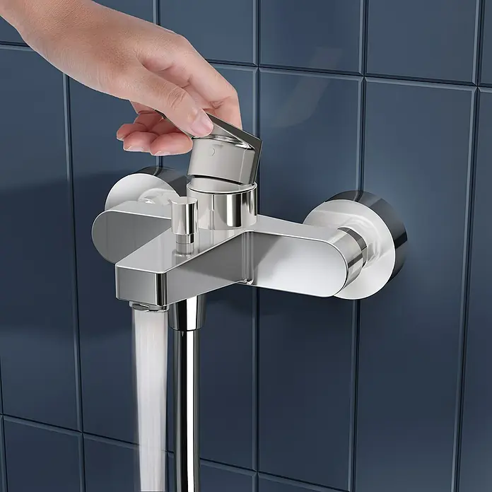 VitrA Flow Square Badewannenarmatur - Chrom, Glänzend - Eine Hand bedient eine verchromte Duscharmatur, installiert an dunkelblauen Fliesen, aus der Wasser fließt.