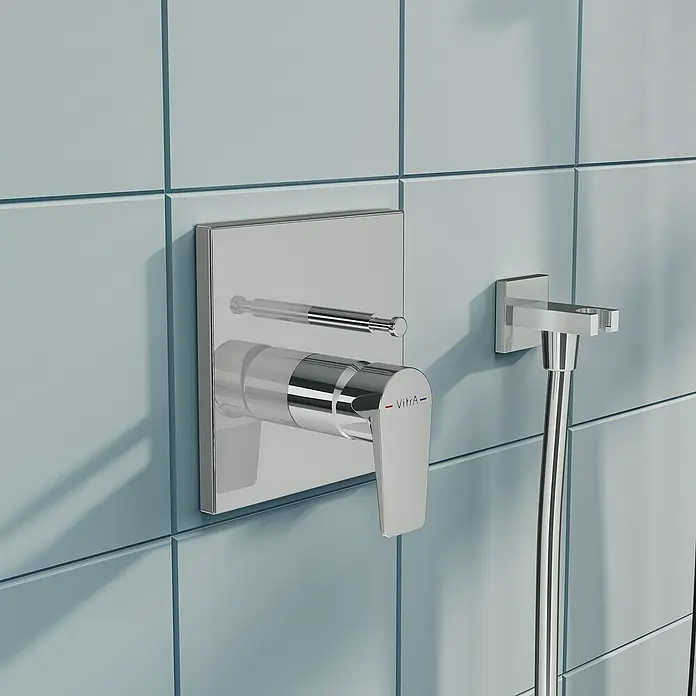 VitrA Flow Square UP-Badewannenarmatur - Ausladung Armatur: 90 mm, Chrom, Glänzend - Verchromte Duscharmatur und Umsteller mit VitrA-Branding und Schlauchhalter, an einer hellblauen Fliesenwand montiert.