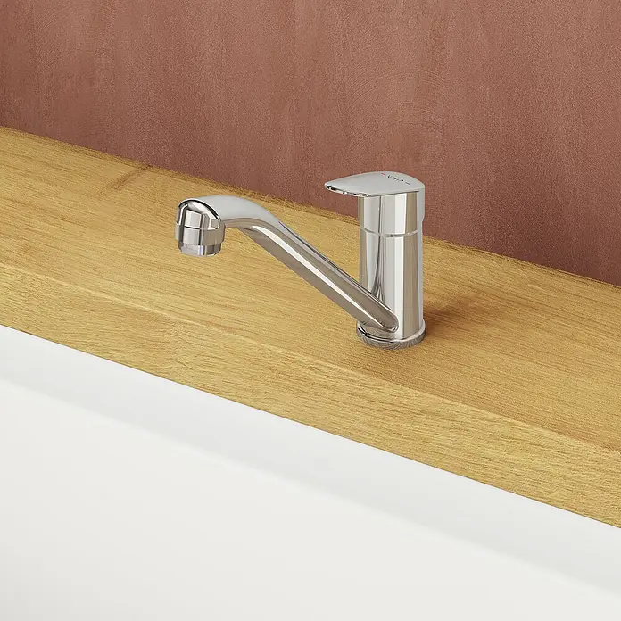 VitrA Flow Round Spültischarmatur - Höhe: 17,4 cm, Chrom, Glänzend - Verchromter Wasserhahn auf Holzarbeitsplatte über weißem Waschbecken vor rostbrauner Wand.