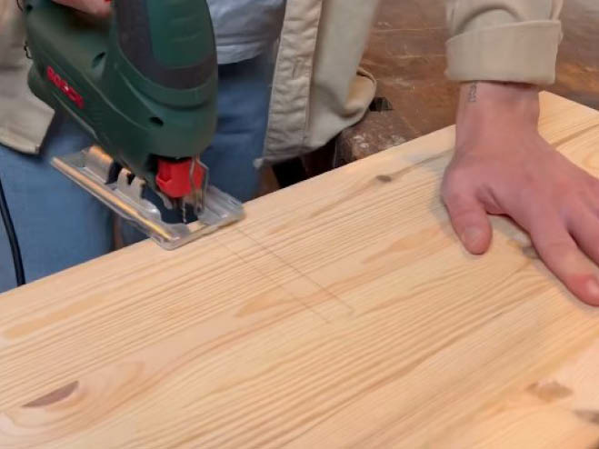 Kleines Holzstück wird mit Stichsäge auf einer Platte geschnitten