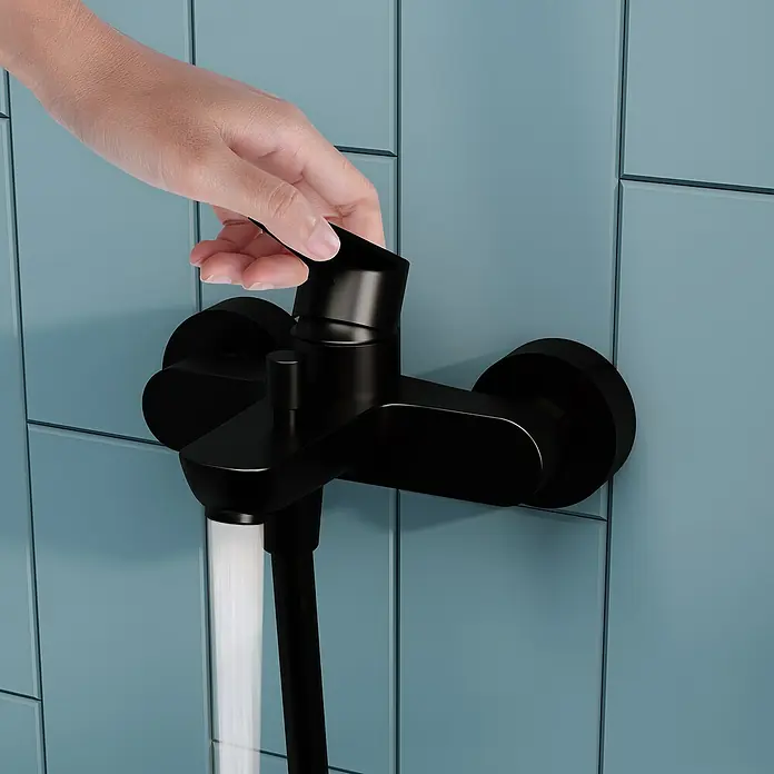 VitrA Flow Soft Badewannenarmatur - Schwarz, Matt - Hand dreht mattschwarze Duscharmatur an blauer Wand, Wasser fließt aus dem Auslauf.