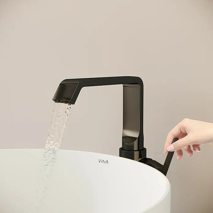 VitrA Suit Waschtischarmatur - Schwarz, Glänzend, Ohne Zugstange, Höhe: 25,7 cm - Moderner schwarzer Wasserhahn, der Wasser in ein weißes Waschbecken spendet, mit einer Hand, die den Hebel bedient.
