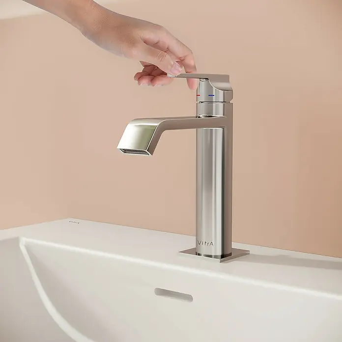 VitrA Suit Waschtischarmatur - Chrom, Glänzend, Höhe: 19 cm - Eine Hand bedient einen modernen VitrA Wasserhahn aus gebürstetem Metall über einem weißen Waschbecken.