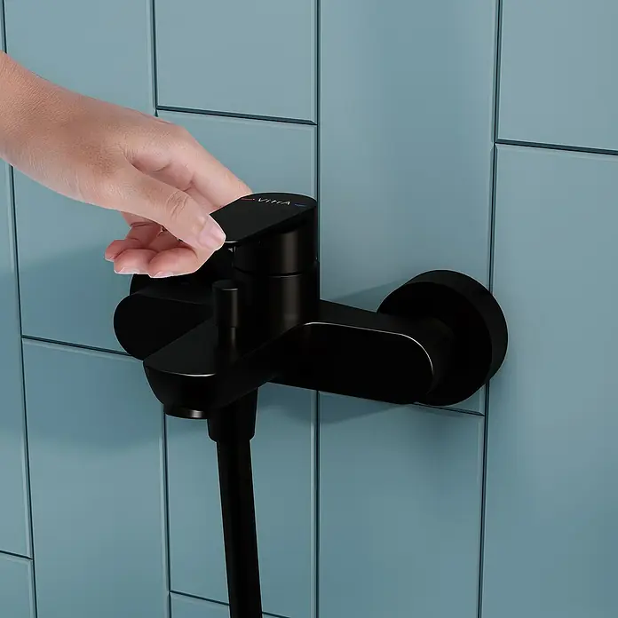VitrA Flow Soft Badewannenarmatur - Schwarz, Matt - Schwarze Duscharmatur, deren Griff von einer Hand an einer blauen Wand verstellt wird.