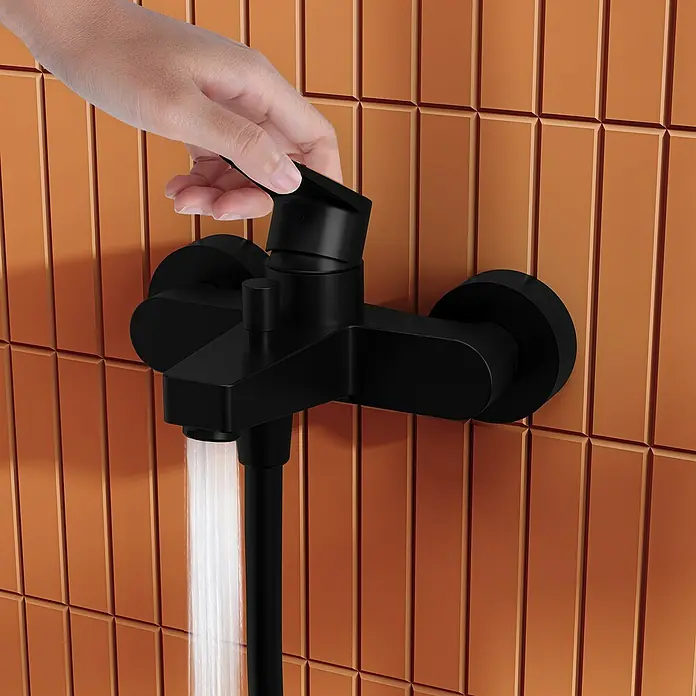 VitrA Flow Square Badewannenarmatur - Schwarz, Matt - Matter schwarzer Duschmischer auf Terrakotta-Fliesen, mit Hand am Hebel und fließendem Wasser.