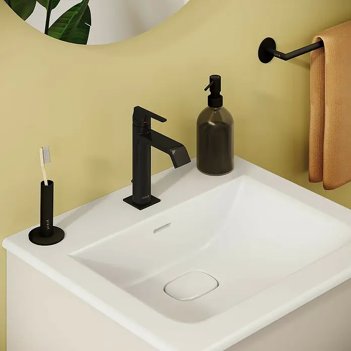 VitrA Suit Waschtischarmatur - Schwarz, Glänzend, Höhe: 19 cm - Moderner VitrA schwarzer Wasserhahn, Seifenspender, Zahnbürstenhalter und Handtuchhalter mit braunem Handtuch auf weißem Waschbecken.
