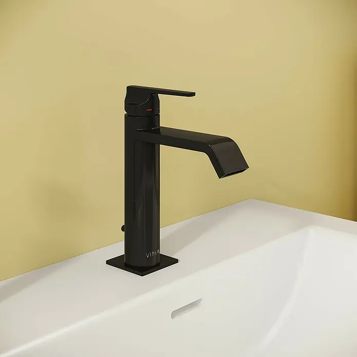 VitrA Suit Waschtischarmatur - Schwarz, Glänzend, Höhe: 19 cm - Glänzender schwarzer Wasserhahn mit rot/blauen Anzeigen auf einem weißen Waschbecken vor gelber Wand.
