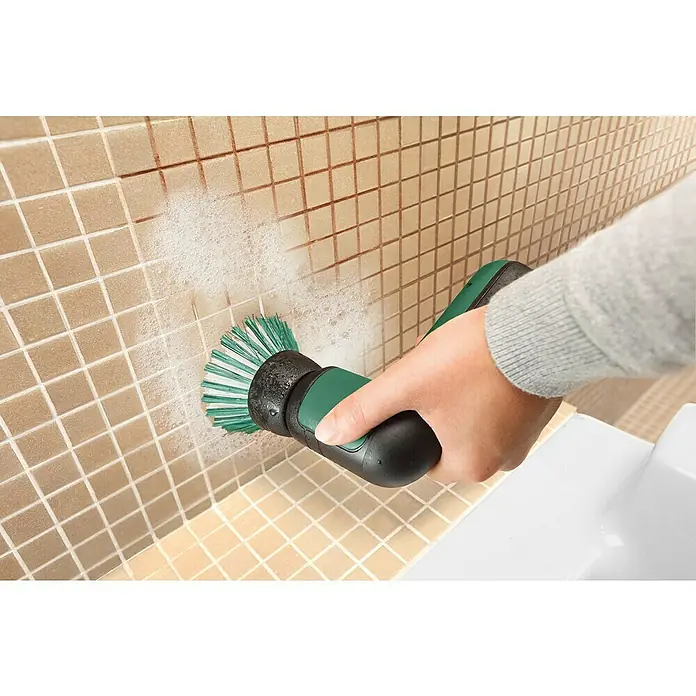 Bosch Softbürste - Passend für: Bosch Akku-Universalbürste UniversalBrush - Hand reinigt hellbraune Fliesenwände mit einer grün-schwarzen Elektrobürste, Seifenschaum ist sichtbar.