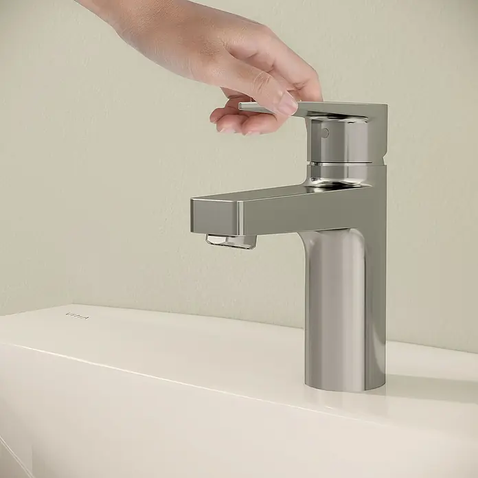 VitrA Flow Square Waschtischarmatur - Chrom, Glänzend, Höhe: 15,6 cm, Mit Zugstange - Hand bedient eine moderne metallische Armatur auf einem hellen Waschbecken.
