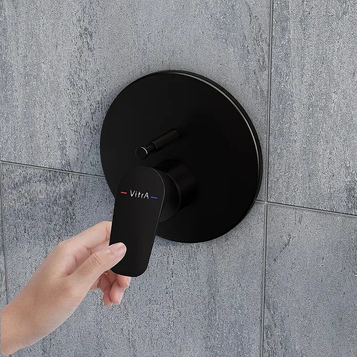 VitrA Flow Soft UP-Badewannenarmatur - Schwarz, Matt, Ausladung Armatur: 87 mm - Mattschwarze VitrA Duscharmatur an einer grauen Fliesenwand, eine Hand verstellt den Hebel.