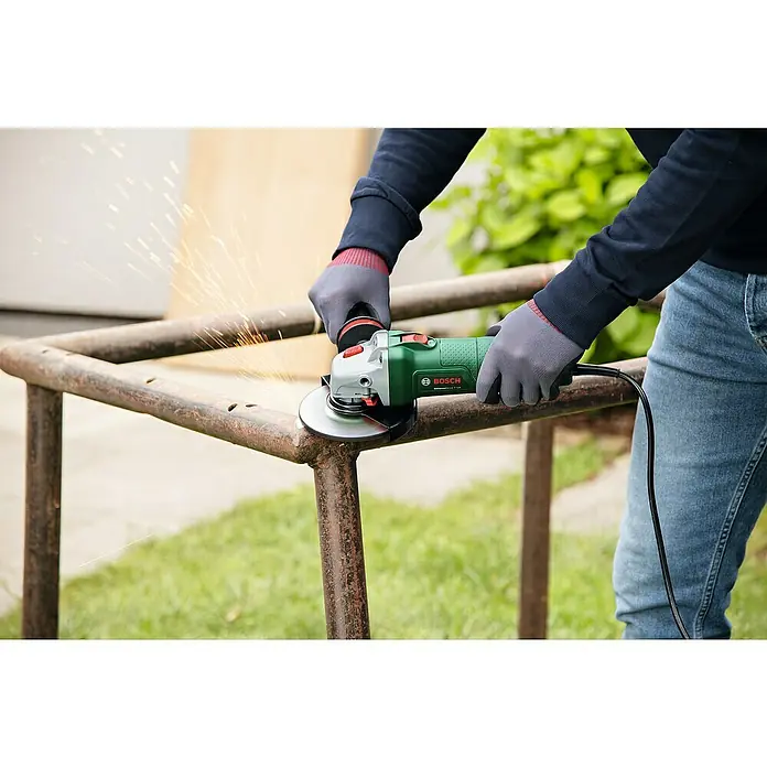 Bosch Elektro-Winkelschleifer UniversalGrind 850-125 - 850 W, Durchmesser Scheibe: 125 mm, Leerlaufdrehzahl: 12.000 U/min - Eine Person schleift Metall mit einem grünen Bosch Winkelschleifer, wobei Funken sprühen. Der Winkelschleifer ist das Hauptaugenmerk des Bildes.
