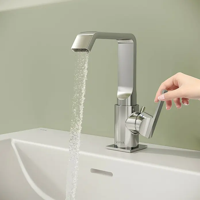 VitrA Suit Waschtischarmatur - Chrom, Glänzend, Mit Zugstange, Höhe: 20,6 cm - Gebürsteter Chrom-Wasserhahn mit fließendem Wasser über einem weißen Waschbecken, von einer Hand bedient.
