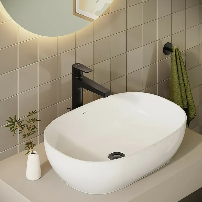 VitrA Flow Square Waschtischarmatur - Schwarz, Matt, Höhe: 30 cm, Mit Zugstange - Ein weißes ovales Aufsatzwaschbecken mit schwarzem Wasserhahn auf heller beiger Arbeitsplatte im modernen Badezimmer.