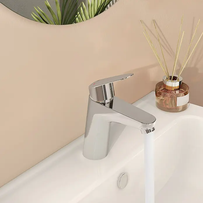VitrA Flow Round Waschtischarmatur - Höhe: 15 cm, Ausladung Armatur: 114 mm, Chrom, Ohne Zugstange - Verchromte Badarmatur mit Wasser, das in ein weißes Waschbecken fließt, in einem modernen Badezimmer.